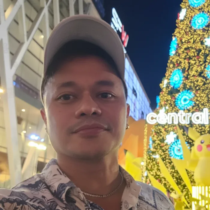 Yong smiling at night in front of a lit-up holiday tree